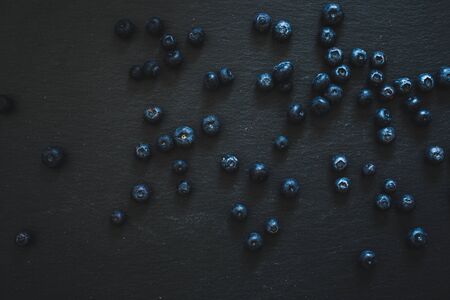 Small blueberries spread all over a dark stone textured slate - Natural fruit background of wild ripe berriesの写真素材