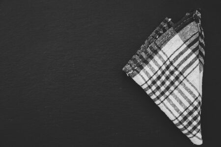 Black and white plaid rustic towel folded in a triangle shape on a black background with copy space...