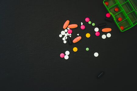 Pills of different colors, sizes and shapes spread on a black background with copy space - Medicines used for treating different illnessesの写真素材