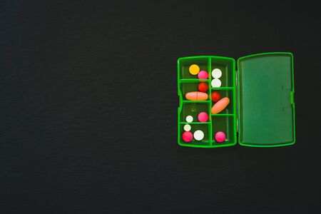 Medicine portions in green plastic case - Pills and tablets in a compartmented box on dark slate background with copy spaceの写真素材