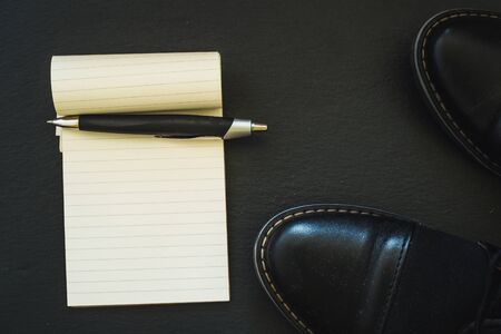 Black leather men shoes with a notebook and pen placed next to them on dark background with copy space - Concept image of time managementの写真素材