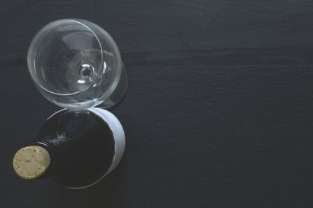 Standing red wine dark bottle with elegant wine glass on black background with copy space - Glass recipients for booze on stone textured tableの写真素材