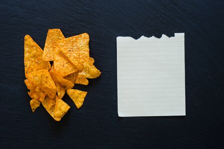 Natural chips and blank piece of paper on a dark table as penguin - tortilla chips and MT sheet of paper with copy spaceの写真素材