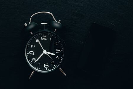 Old alarm clock with green pill case on black desk as backgrounds - vintage bell clock and medicine organizer placed on dark stone surfaceの写真素材