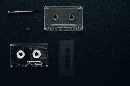 Minimalist flat lay of opened retro cassette with small screwdriver on black background with copy space - Vintage audio device used to record music on it - old fashioned plastic tapeの写真素材