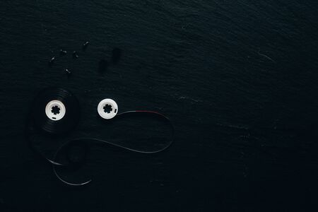 Old fashion audio tape unfolded on a dark stone surface with copy space - Vintage plastic audio device used for sound recording on clack backgroundの写真素材