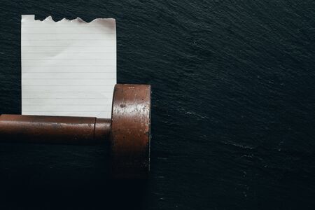 Old and rusty dumbbell with small  blank piece of paper on dark table as background with copy space...