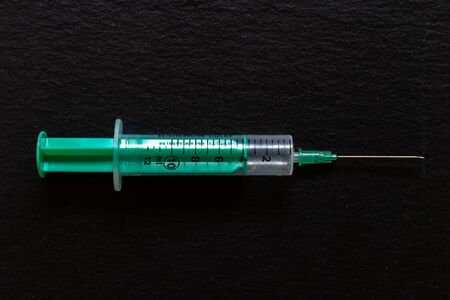 Green and transparent syringe with needle placed on black background in a horizontal position...