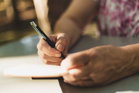 Woman taking notes with black pen in small notebook outdoors - Close-up shot of people writing information in agenda while sitting in a parkの写真素材