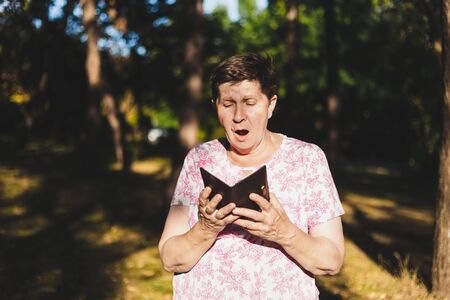 Surprised and happy senior woman holding a wallet while looking inside it outdoors - Cheerful old lady checking the money and credit cards - Concept image for discountsの写真素材