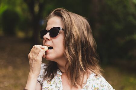 Portrait of a young woman eating a garlic clove outdoors - Casually dressed woman wearing sunglasses...