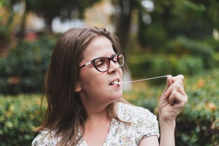 Beautiful teenager wearing eyeglasses having fun while playing with chewing gum outdoors - Portrait...