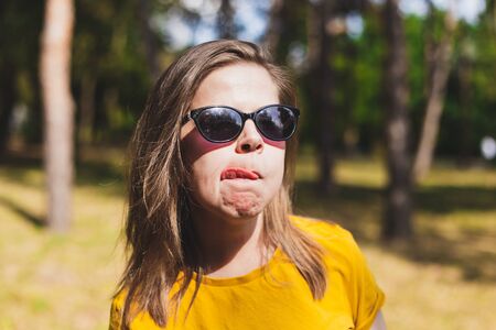 Happy beautiful young woman showing tongue outdoors - Casually dressed millennial girl wearing sunglasses being funny and feeling good while spending time in the park on a sunny dayの写真素材