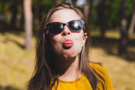 Ruse young woman acting childish while showing tongue outdoors - Beautiful millennial wearing summer outfit and sunglasses feeling angry and - Cute female being silly in natureの写真素材