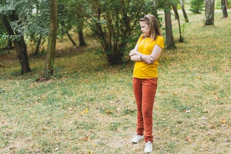 Worried young woman standing alone in the forest while looking down - Casually dressed girl holding her arms crossed feeling abandoned in nature - Concept image for paranoiaの写真素材