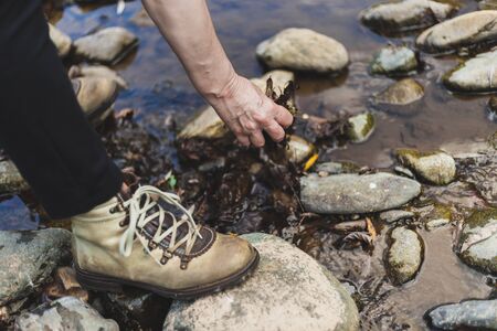 Hiking woman playing with some rocks by the river in nature on a sunny day - Elderly person feeling...
