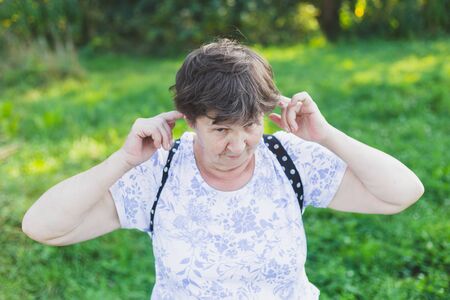Happy smiling senior woman acting silly outdoors - Cute old lady having fun and feeling good while playing with her ears in nature - Elderly person with healthy and balanced mental lifestyleの写真素材