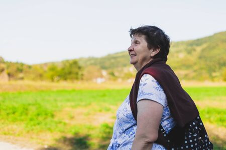 Smiling senior woman walking in nature on a sunny day - Calm old lady going on an adventure in the woods - Relaxing and peaceful activity for elderly people during holidaysの写真素材