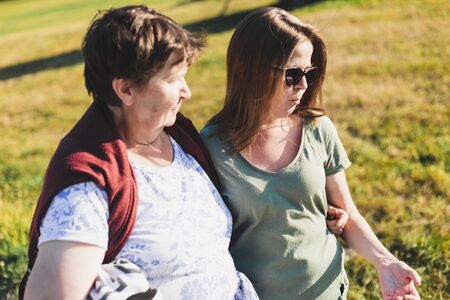 Portrait of mother and daughter sitting and talking outdoors on a sunny day - Casually dressed girl wearing sunglasses and cute old lady discussing in natureの写真素材