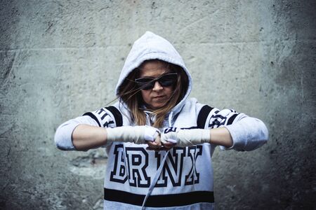 Smiling girl fighter with white hoodie wearing sunglasses holding her fists together standing in the...