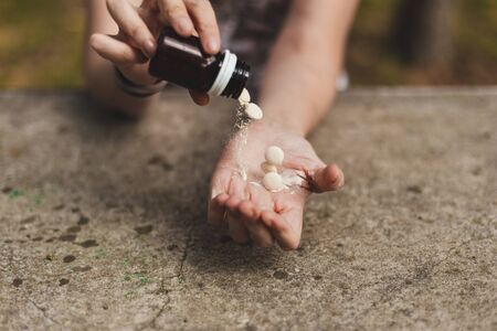 Young personâ€™s hand pouring out pills from bottle outdoors - Sick woman taking drugs from a...