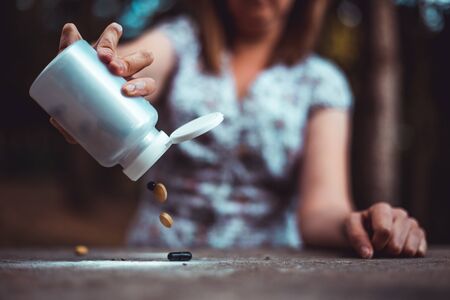 Young personâs hand pouring out pills from white plastic container - Woman taking vitamins and supplements - Synthetic pharmaceutical medicine used in various situationsの写真素材