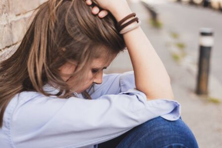 Sad and depressed young female holding her head in one hand outdoors - Side view of beautiful upset...
