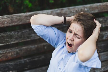 Afraid woman screaming while holding both hands on her head in a park - Stressed girl with tens face...