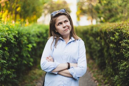 Doubtful young woman looking up with wonder outdoors - Portrait of curious girl with brown hair casually dressed standing in the park - Pretty female questioning thingsの写真素材
