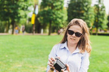 Young woman holding portable speaker in the park on a sunny day - Casually dressed girl wearing sun...