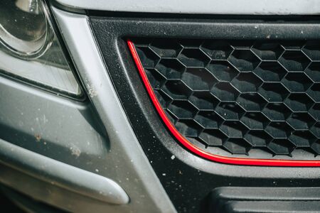 Black grid with red line on a grey car - Hexagonal shaped grille of a modern sport vehicle - Daek automotive aftermarket part made of plasticの写真素材