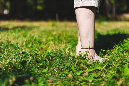 Young person standing with feet in the grass on a sunny day - Girl wearing brown bracelet on her...