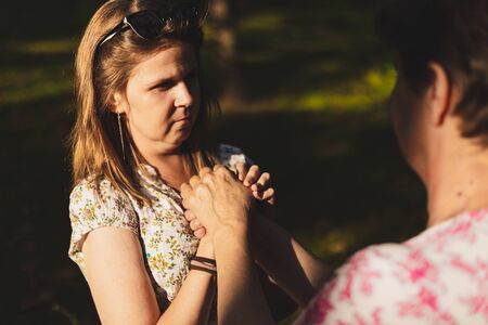 Young female holding seniorâs hand for support outdoors - Casually dressed girl offering help to elderly woman in the park - Pretty emphatic lady with brown hair showing affection to an older personの写真素材