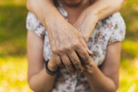 Mother holding arm over her daughter's shoulders outdoors - Loving parent hands protecting and...