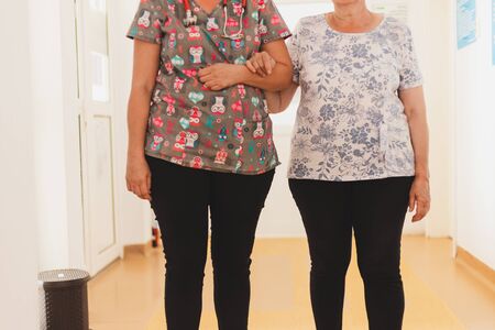 Nurse helping and holding senior woman while waking in the hospital - Female medical assistant offering support to elderly person in a private clinic - Concept image for helping othersの写真素材