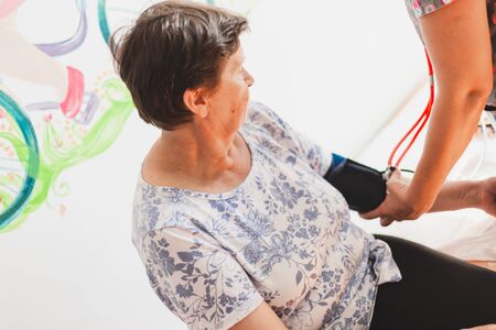 Female nurse taking blood pressure from senior woman in the hospital - Doctor with stethoscope checking vital signs of cute old lady in a private clinicの写真素材