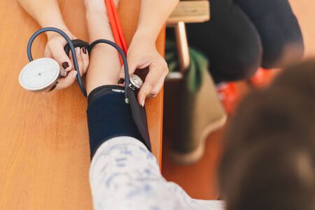 Nurse taking blood pressure from a young woman with stethoscope in the hospital - Female medical assistant checking vital signs and health of a patient in a private clinicの写真素材