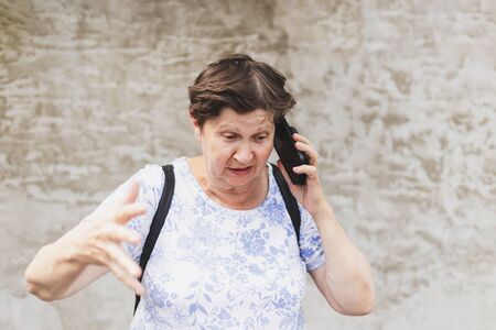 Angry senior woman talking and yelling on the mobile phone outdoors - Old lady getting mad while discussing on the telephone - Elderly person using modern wireless technologyの写真素材