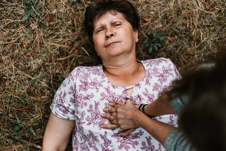 Person performing CPR to senior woman lying down in the park - Young female giving first aid to old lady suffering from heart problems outside - Sick elderly person fallen on the groundの写真素材