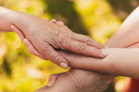Close-up shot of mother and daughter holding hands outside in the sun - Young woman hand holding...