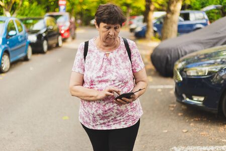 Serious senior woman using a mobile phone outside - Cute old lady holding a cellphone while texting...