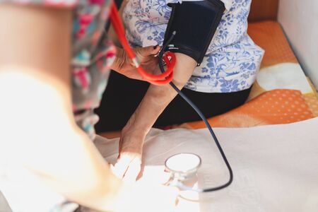 Close-up shot of female nurse taking blood pressure from senior woman in a hospital - Young doctor checking health condition of old lady in a private clinic - Concept image for health careの写真素材