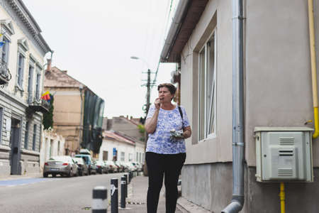 Senior woman eating chocolate while walking on the sidewalk - One old person biting and enjoying a cocoa bar outsideの写真素材