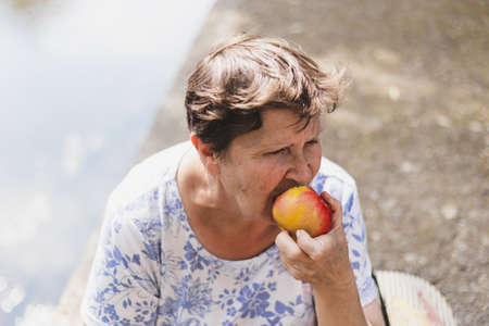 Senior eating apple outside - Portrait of a grandmother sitting and enjoying a nutritious fruit as snackの写真素材