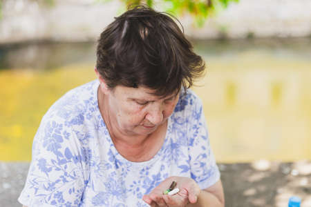 Senior woman holding pills while looking at them outdoors - Cute old lady with brown hair taking vitamins and supplements for a healthy lifestyle - Concept image for addictionの写真素材