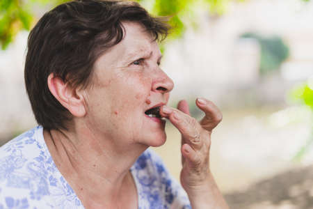 Old woman eating chocolate - Senior preparing biting or putting a piece of sweet snack into her open mouthの写真素材