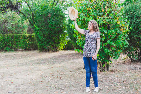 Waving goodbye - Woman greeting with straw hat in raised hand - Lovely girl welcoming in standing positionの写真素材
