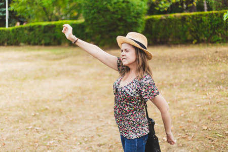 Young woman waving hand - Girl with straw hat and a floral shirt greeting someone that is arriving or leavingの写真素材