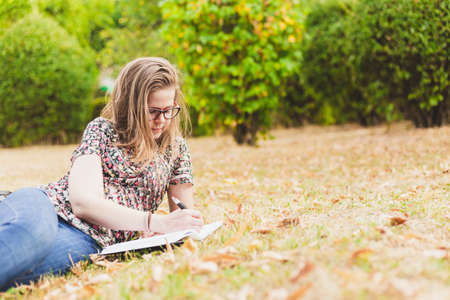 Woman writing outside - Student studying outside in college campus laying on the side in grass while wearing eyeglassesの写真素材