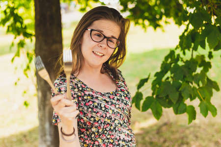 Happy young woman playing with metallic forks outside on a summer day - Pretty girl with eyeglasses having fun and acting silly holding kitchen utensils in the parkの写真素材